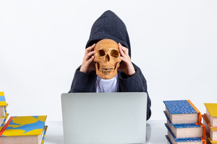 Person with skull mask using laptop for ghostwriting concept