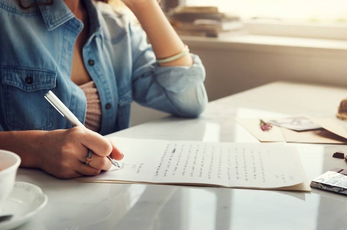 Student writing study notes in notebook at computer desk