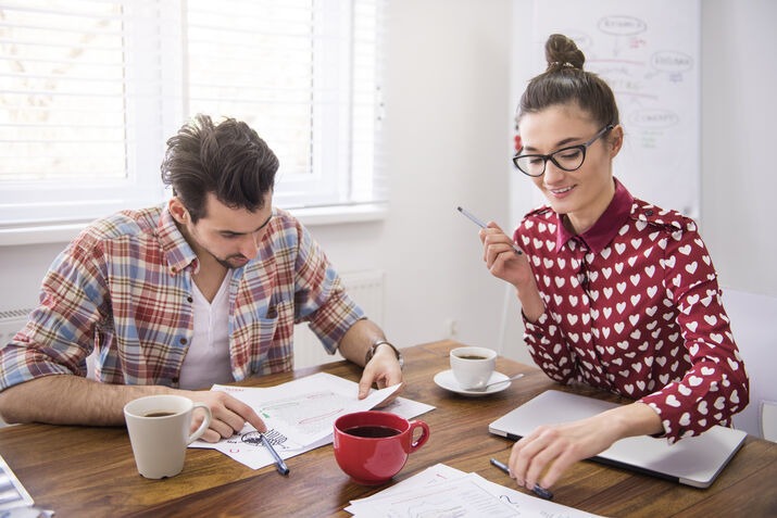Two writers reviewing documents and discussing edits at a workspace.