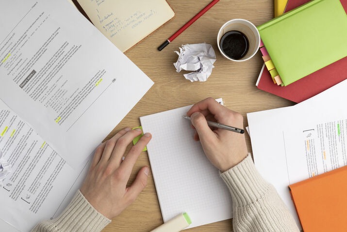 Writer taking notes on a desk with documents, notebooks, and coffee.